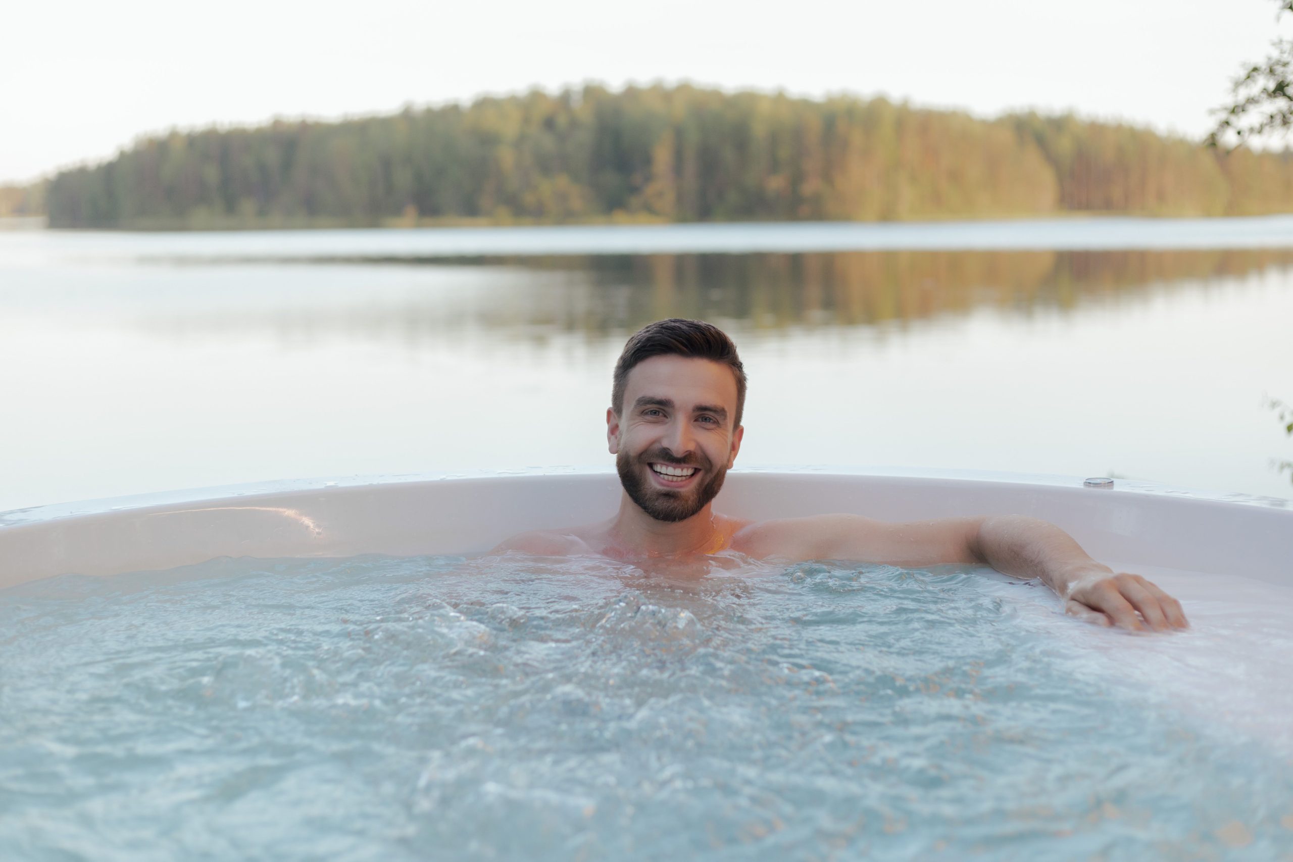 Homme souriant dans un spa extérieur au bord du lac
