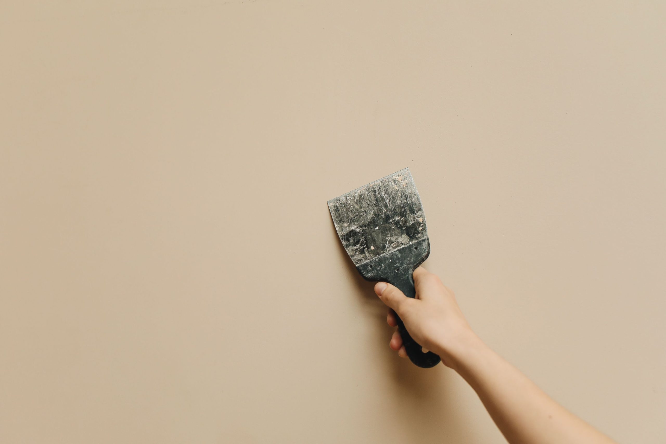Main tenant une spatule sur mur beige