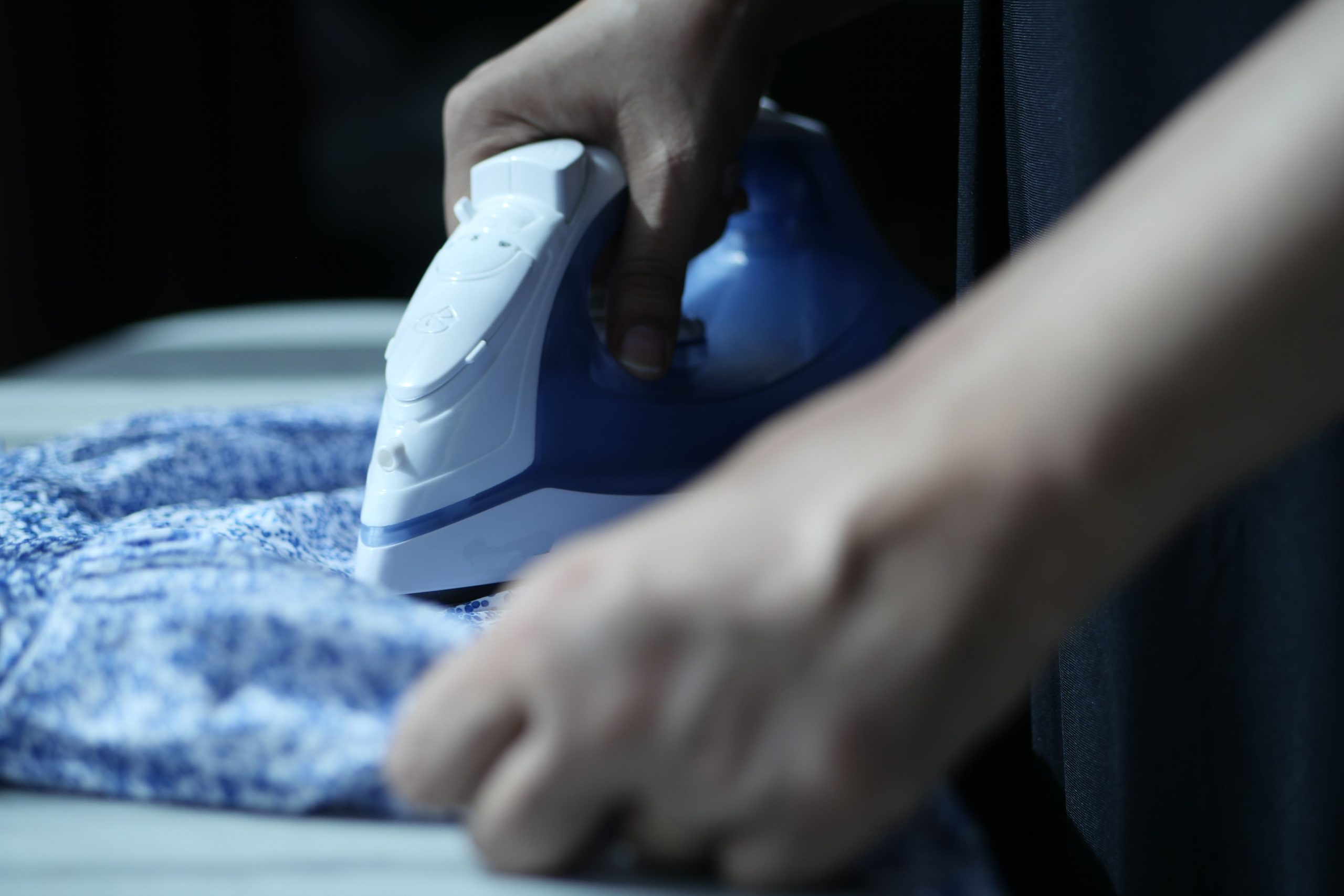 Mains utilisant un fer électrique sur tissu bleu